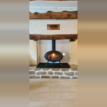 Poêle à bois INVICTA BRIO installé dans une ancienne cheminée, sur plaque de sol noire