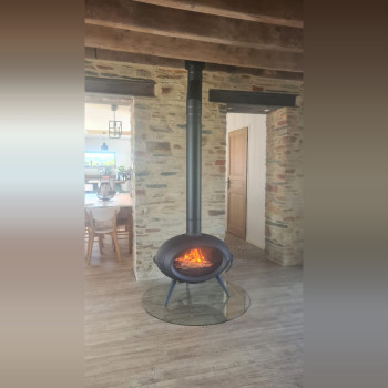Poêle à bois INVICTA BRIO au centre d'une pièce en pierre, sur plaque de protection en verre